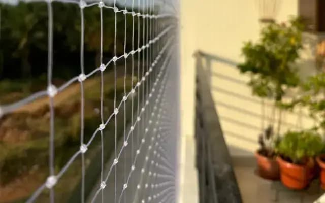 Close view of clear square-mesh netting beside a balcony railing and potted plants